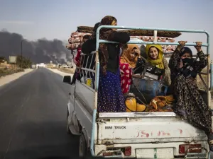Displaced people, fleeing from the countryside of the Syrian Kurdish town of Ras al-Ain along the border with Turkey, ride in the back of a pickup truck along a road on the outskirts of the nearby town of Tal Tamr on October 16, 2019 as they flee a deadly cross-border Turkish offensive that has sparked an international outcry, with smoke plumes of tire fires billowing in the background to decrease visibility for Turkish warplanes in the area. Delil SOULEIMAN / AFP