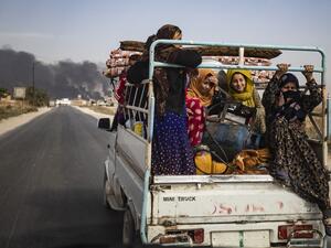 Displaced people, fleeing from the countryside of the Syrian Kurdish town of Ras al-Ain along the border with Turkey, ride in the back of a pickup truck along a road on the outskirts of the nearby town of Tal Tamr on October 16, 2019 as they flee a deadly cross-border Turkish offensive that has sparked an international outcry, with smoke plumes of tire fires billowing in the background to decrease visibility for Turkish warplanes in the area. Delil SOULEIMAN / AFP