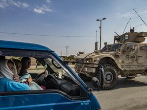 A US military vehicle drives on a road after US forces pulled out of their base in the Northern Syriain town of Tal Tamr on October 20, 2019, as members of a Syrian family fleeing the countryside of Ras al-Ain head north in a van to the region of al-Hasakeh. US forces withdrew from a key base in northern Syria today, a monitor said, two days before the end of a US-brokered truce to stem a Turkish attack on Kurdish forces in the region. Delil SOULEIMAN / AFP