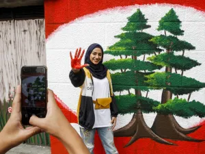 A woman shows her red-painted hand as she poses for a picture next to a mural depicting two cedars during a demonstration in southern city of Sidon on the seventh day of protest against tax increases and official corruption, on October 23, 2019. Mahmoud ZAYYAT / AFP