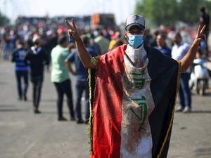 An Iraqi protester, draped in a national flag, flashes the victory sign near the capital Baghdad's Al-Jumhuriyah Bridge on October 26, 2019, during an anti-government rally. Iraqi security forces fired tear gas to clear lingering protesters in Baghdad this morning, after dozens died in a bloody resumption of anti-government rallies to be discussed in parliament. (AFP)