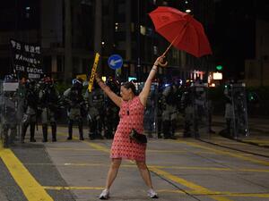 A woman holds up an umbrella and license plates, one that reads 'angel', as she stands in front of a row of riot police during violent clashes with demonstrators in the Causeway Bay district of Hong Kong on October 1, 2019. (AFP/ File Photo)