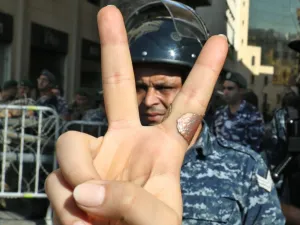 A Lebanese protester flashes the victory gesture while standing before a riot policeman at a security barrier across a road leading to the parliament headquarters during a demonstration in the capital Beirut's downtown district on November 19, 2019. An unprecedented protest movement against the ruling elite entered its second month with the country in the grip of political and economic turmoil. The leaderless pan-sectarian movement has swept the Mediterranean country since October 17, prompting the resignat