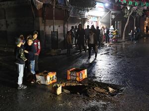 Syrian children stand around a whole on the road following a reported rocket attack in the government-held northern city of Aleppo on November 21, 2019. AFP