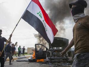 Iraqi demonstrators stand next to the smoking remains of an Iraqi anti-riot vehicle during a demonstration in the southern city of Basra on November 24, 2019, as protesters cut-off roads and activists call for a general strike.  (AFP/ File Photo)