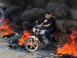 An Iraqi man drives through burning tires in the Shiite Muslim shrine city of Karbala, south of Iraq's capital Baghdad, on November 26, 2019. Since October 1, Iraq's capital and majority-Shiite south have been swept by mass rallies against corruption, a lack of jobs and poor services that have escalated into calls for a complete overhaul of the ruling elite. Mohammed SAWAF / AFP