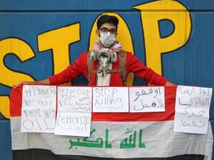 An 18-year-old Iraqi student wearing a surgical mask and a gas mask around his neck poses for a picture while holding up a national flag covered with messages in English and Arabic, during an anti-government demonstration in the capital Baghdad on November 21, 2019.  (AFP/ File Photo)