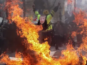 A Yellow Vest protester wearing a mask depicting the French President on which is written 'psycho', gestures behind flames rising from barricades, in Paris on March 16, 2019, during the 18th consecutive Saturday of demonstrations called by the 'Yellow Vest' (gilets jaunes) movement. (AFP/ File Photo)
