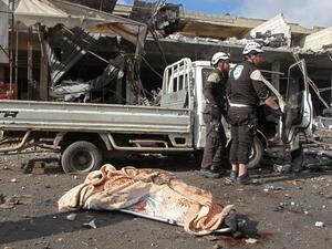The body of a victim lies on the ground near members of the Syrian Civil Defence (White Helmets) following a regime air strike on December 2, 2019 in a market in the town of Maaret al-Numan in the jihadist-run Syrian province of Idlib. Regime air strikes killed 10 civilians and wounded at least 15 in Syria's last major opposition bastion, where deadly clashes between regime forces and armed groups have escalated in the past two days, the Britain-based Syrian Observatory for Human Rights added said. Abdulazi