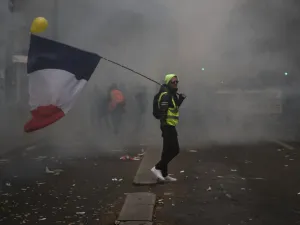 A man holding a French flag and a yellow vest walks in tear gas during a demonstration against the pension overhauls, in Paris, on December 5, 2019 as part of a nationwide strike. Trains cancelled, schools closed: France scrambled to make contingency plans on for a huge strike against pension overhauls that poses one of the biggest challenges yet to French President's sweeping reform drive. Zakaria ABDELKAFI / AFP