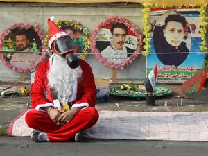 An Iraqi demonstrator wearing a Santa Claus costume and a gas mask sits on a blanket in the capital Baghdad's Tahrir Square, amid ongoing anti-government protests, on December 6, 2019.  (AFP/ File Photo)