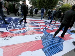 Supporters of Asaib Ahl al-Haq, a faction of Iraq's Popular Mobilization Units (PMU), walk over a makeshift US flag during a demonstration against US sanctions on its leader Qais Khazali, in the Iraqi capital's Karrada district on December 14, 2019. (AFP)