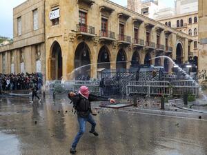 An anti-government protester throws a rock at security forces as they fire water cannon from behind a barrier during clashes in the central downtown district of the Lebanese capital Beirut near the parliament headquarters on January 18, 2020. ANWAR AMRO / AFP