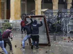 Anti-government protesters use a window as a makeshift shield as they confront security forces from behind a barbed-wire and metal fence barrier during clashes in the central downtown district of the Lebanese capital Beirut near the parliament headquarters on January 18, 2020. ANWAR AMRO / AFP