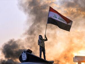An anti-government protester waves a national flag as he stands above a statue of a policeman's hat during a demonstration in the central Iraqi holy shrine city of Najaf on January 19, 2020. Haidar HAMDANI / AFP