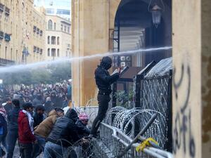 An anti-government protester displays the middle-finger gesture as security forces spray water cannon at demonstrators during clashes in the central downtown district of the Lebanese capital Beirut near the parliament headquarters on January 18, 2020. Anwar AMRO / AFP