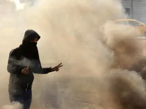 A masked anti-government protester gestures the victory sign as he runs from tear gas fired by security forces during clashes in the central Iraqi holy shrine city of Karbala on January 20, 2020. Mohammed SAWAF / AFP