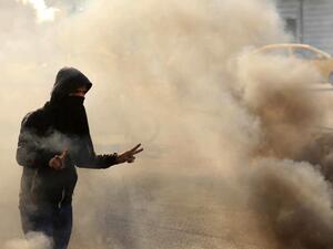 A masked anti-government protester gestures the victory sign as he runs from tear gas fired by security forces during clashes in the central Iraqi holy shrine city of Karbala on January 20, 2020. Mohammed SAWAF / AFP