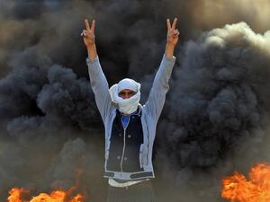 A masked anti-government protester flashes the victory gesture as he stands before flaming tyres at a make-shift roadblock in the central Iraqi holy shrine city of Najaf on January 27, 2020. Haidar HAMDANI / AFP