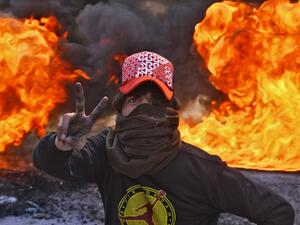 A masked anti-government protester flashes the victory gesture as he stands before flaming tyres at a make-shift roadblock in the central Iraqi holy shrine city of Najaf on January 27, 2020. Haidar HAMDANI / AFP