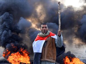An anti-government protester draped in a national flag chants slogans while holding a stick at a make-shift roadblock with flaming tyres during a demonstration against the new Iraqi prime minister designate in the central holy shrine city of Najaf on February 2, 2020. AFP