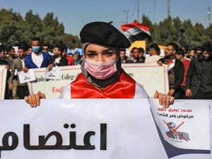 An Iraqi student wearing a beret and a surgical mask holds signs with a red X mark on the face of the new Iraqi prime minister designate Mohammad Allawi reading in Arabic "rejected by order of the people" during a demonstration against him in the central holy shrine city of Karbala on February 2, 2020. Mohammed SAWAF / AFP