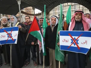 Palestinian protesters stand with Palestinian and Hamas (green) flags and hold up signs showing the Israeli flag defaced with a red X mark and with words in Arabic reading "to demise" during a demonstration against US President Donald Trump's Middle East peace proposal in Khan Yunis in the southern Gaza Strip on February 3, 2020. SAID KHATIB / AFP