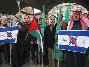 Palestinian protesters stand with Palestinian and Hamas (green) flags and hold up signs showing the Israeli flag defaced with a red X mark and with words in Arabic reading "to demise" during a demonstration against US President Donald Trump's Middle East peace proposal in Khan Yunis in the southern Gaza Strip on February 3, 2020. SAID KHATIB / AFP