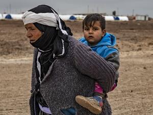A Syrian woman walks by carrying a child on her back in the Washukanni Camp for the internally displaced, near the predominantly Kurdish city of Hasakeh in northeastern Syria, on February 17, 2020. Delil SOULEIMAN / AFP