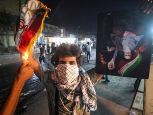 In this file photo taken on September 07, 2018, an Iraqi protester holds up an Iranian flag as another sets it on fire for him, next to a portrait depicting Iran's former and current Supreme Leaders Ayatollah Khomeini and Khamenei, during demonstrations against the government and the lack of basic services in Basra. Mocking clerics, falling in love at rallies and mending a broken society: even if Iraq's young protesters have failed to overthrow entrenched politicians, they have scored by shattering decades-