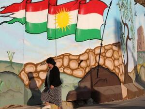 A woman walks passed a mural depicting the Kurdish flag in Erbil. (AFP)