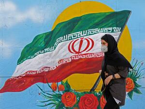 Iranians wearing masks walk past a mural displaying their national flag in Tehran on March 4, 2020. Iran has scrambled to halt the rapid spread of the COVID-19 virus, shutting schools and universities, suspending major cultural and sporting events, and cutting back on work hours.  ATTA KENARE / AFP