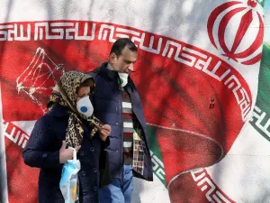 Iranians wearing masks walk past a mural displaying their national flag in Tehran on March 4, 2020. Iran has scrambled to halt the rapid spread of the COVID-19 virus, shutting schools and universities, suspending major cultural and sporting events, and cutting back on work hours.  ATTA KENARE / AFP