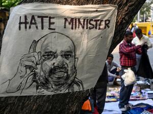 A street vendor selling clothes stands behind a poster displaying a drawing of Home Minister Amit Shah (L) during a protest against India's new citizenship law in New Delhi on March 4, 2020. Sajjad HUSSAIN / AFP