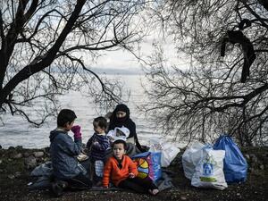 A family sits on a blanket near the yard of a small church where they spent the night after arriving last night near Skala Sykamnias on the Greek island of Lesbos on March 6, 2020. A group of 42 refugees and migrants managed to by pass coast guard patrols and landed on the shores of Lesbos in the evening of March 5. LOUISA GOULIAMAKI / AFP