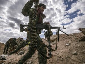 In this file photo taken on March 17, 2019, a fighter of the Syrian Democratic Forces (SDF) walks carrying a machine gun at a position close to the camp of Baghouz where remaining Islamic State (IS) group fighters and their families are holding out in the last position controlled by IS, awaiting to advance on them in the countryside of the eastern Syrian province of Deir Ezzor. As it enters its tenth year, the war in Syria is anything but abating as foreign powers scrap over a ravaged country where human su