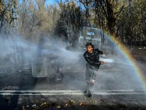 A migrant runs away as another one takes cover behind a trash container as Greek police uses water cannons to block them trying to break fences in the Turkey-Greece border province of Edirne on March 7, 2020 as makeshift camps have sprung up around the border where thousands of refugees have been encouraged by Turkey to leave for the European Union, in a bid to gain Western backing in Syria. As part of the 2016 agreement, Turkey agreed to stop the flow of migrants to Europe in exchange for billions of euros