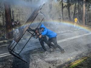 Migrants take cover behind a wooden board as Greek police uses water cannons to block them trying to break fences in the Turkey-Greece border province of Edirne on March 7, 2020 as makeshift camps have sprung up around the border where thousands of refugees have been encouraged by Turkey to leave for the European Union, in a bid to gain Western backing in Syria. As part of the 2016 agreement, Turkey agreed to stop the flow of migrants to Europe in exchange for billions of euros, but Ankara accused the Europ