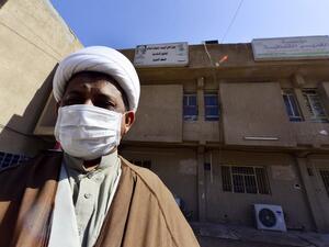 A cleric wearing a protective mask stands outside the building of a religious school which attracts predominantly foreign students and where the first Iraqi case of novel coronavirus infection was confirmed, during its disinfection in the central Iraqi shrine city of Najaf, on March 9, 2020. Haidar HAMDANI / AFP