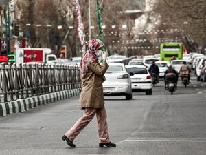 A woman wearing a protective face mask and latex gloves crosses a street in Iran's capital Tehran on March 14, 2020. STRINGER / AFP