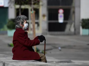 In this file photo taken on March 08, 2020 an elderly woman wearing a protective face mask sits on a bench in the city centre of Milan, after millions of people were placed under forced quarantine in northern Italy as the government approved drastic measures in an attempt to halt the spread of the COVID-19 outbreak, caused by the novel coronavirus that is sweeping the globe. While Italy is a country of senior citizens, the oldest in Europe according to statistics, and few of them live in retirement homes, t