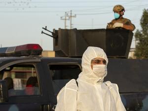 A member of the Iraqi security forces stands guard atop a military vehicle as a health worker wearing a protective outfit walks by during a curfew imposed as a measure to stem the spread of the novel coronavirus in the southern city of Basra on March 19, 2020. The US-led coalition is temporarily withdrawing training forces from Iraq as a protective measure against the novel coronavirus, a senior official in the alliance said today. Iraqi health officials have confirmed 13 deaths and more than 170 cases of C