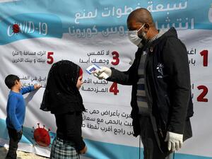 A medical volunteer takes the temperature of a displaced Syrian girl next to a poster, outlining 7 steps to prevent the spread of CONVID-19, at a camp for the internally displaced near Dayr Ballut, near the Turkish border in the rebel-held part of Aleppo province on March 22, 2020, during a campaign to prevent the spread of the virus. Rami al SAYED / AFP
