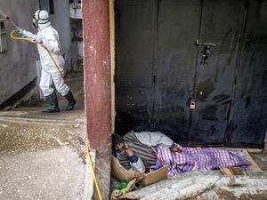 A homeless man sleeps on the side of a road as a Moroccan health ministry worker disinfects the wall of a building in the capital Rabat on March 22, 2020. A public health state of emergency went into effect in the Muslim-majority country late on March 20, and security forces and the army have been deployed on the streets to combat the spread of COVID-19 coronavirus disease. People have been ordered to stay at home, and restrictions on public transport and travel between cities are also in place. FADEL SENNA
