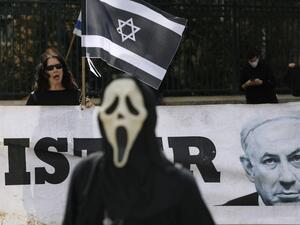 A person wearing a ghost-face mask walks past an Israel woman holding her national flag in black colour motifs, standing behind a portrait of Prime Minister Benjamin Netahyahu, during a protest outside the Knesset (parliament) in Jerusalem on March 23, 2020 against the recent decision by Knesset speaker to shut it down, and against what they describe as "damaged to Israel's democracy". MENAHEM KAHANA / AFP