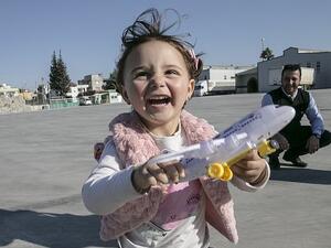 Syrian girl Salwa laughs with her new toys at the Cilvegozu border crossing in Hatay, Turkey (Dailymail)
