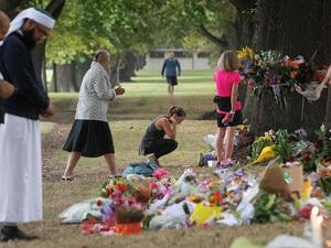 People on Tuesday stand next to floral tributes placed across the road from the Al Noor Mosque in Christchurch, New Zealand, where dozens of worshippers were gunned down last week. (Marty Melville/AFP/Getty Images)