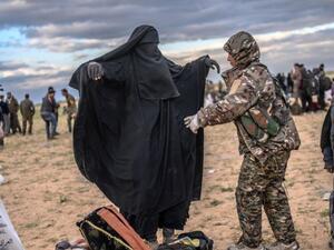 مقاتلة من "قسد" تفتش امرأة من عوائل داعش بأحد معسكرات الاحتجاز في سوريا