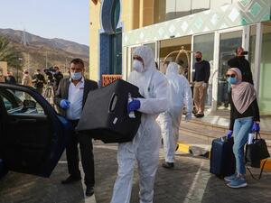 A worker helps a mask-clad woman with her baggage as she prepares to leave a Dead Sea resort where she has been quarantined for 14 days, approximately 60 kilometres sout of the Jordanian capital Amman on March 30, 2020. AFP/File