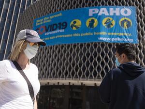 People wearing masks walk past a coronavirus awareness sign outside the World Health Organization in Washington, DC on March 30, 2020. The novel coronavirus, which has infected at least 155,252 people in the US, is thought to have been transmitted to humans by pigs, civets, or pangolins at the Huanan Seafood Wholesale Market in Wuhan, China. ANDREW CABALLERO-REYNOLDS / AFP